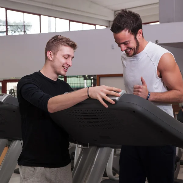 Jovem e instrutor treinando no ginásio com bicicleta . — Fotografia de Stock