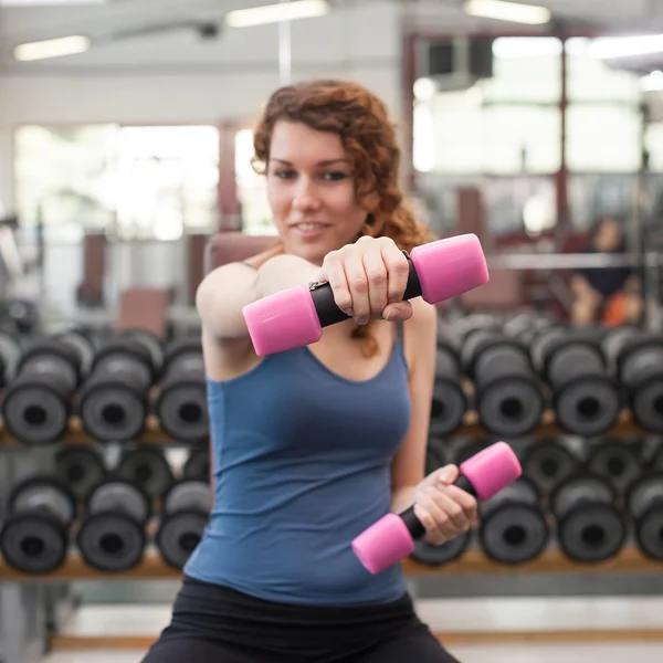 Spor salonunda dambıllarla egzersiz yapan genç bir kadın.. — Stok fotoğraf