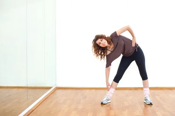 Jonge vrouw die zich uitstrekt van haar been in de sportschool. — Stockfoto