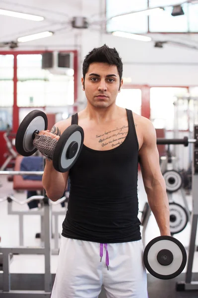 Joven haciendo ejercicio con pesas en un gimnasio . — Foto de Stock