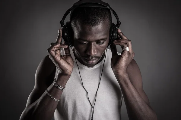 Afrikaanse man met oor-telefoons geïsoleerd op donkere achtergrond. — Stockfoto