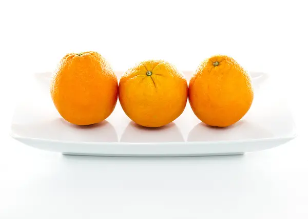 Naranjas sobre plato blanco sobre fondo blanco —  Fotos de Stock