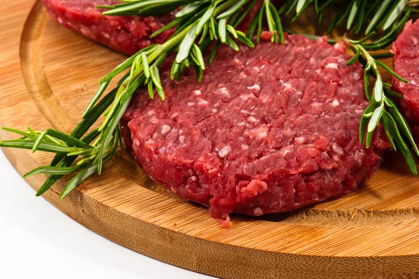 Hamburger crudi con cellophane e rosmarino su tavola di legno — Foto Stock