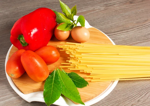 Espaguete, macarrão sobre a mesa com ovos, tomates e pimentas sobre um fundo branco — Fotografia de Stock
