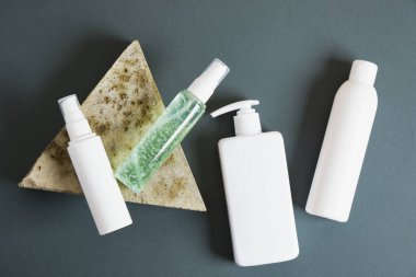 Üçgen taş ve koyu yeşil arka planda beyaz kozmetik şişeler. Etiketsiz birkaç kozmetik paket. üst görünüm kopyalama alanı