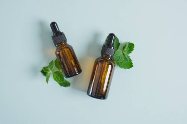 Kehribar cam damlası şişeleri ve nane yaprakları, pipetli nane yağı aromaterapide nane yağı kullanımı ve kozmetik ürünleri taklit ediyor.