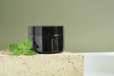 Kozmetik siyah krema kavanozu ve üçgen taşlı açık mavi arka planda taze nane şekeri. Organik kozmetik konsepti. Doğal kozmetik ürün konsepti. Nane yağlı cilt bakım ürünü