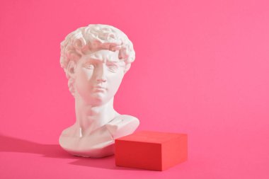 Beyaz dekoratif heykel büstü ve pembe arka plan geometrik şekilli birkaç pembe geometrik bardak altlığı. Sergi podyumu, ürün sunumu platformu