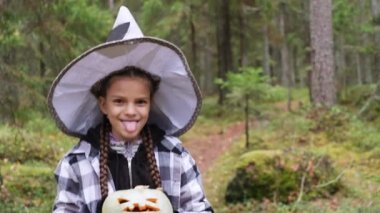 Ekose gömlekli ve cadı şapkalı neşeli kız ormanda elinde bir balkabağı feneri tutuyor. Cadılar bayramı arifesinde kız eğleniyor.