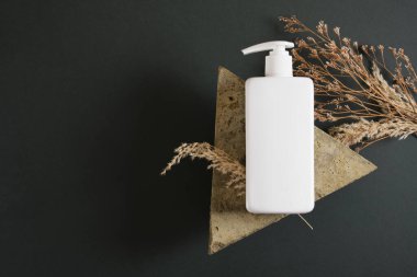 Kuru kuraklık, üçgen taş ve koyu yeşil arka planda beyaz kozmetik şişe. Etiketsiz kozmetik paket. üst görünüm kopyalama alanı