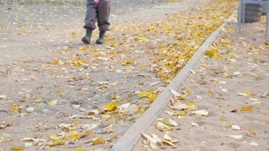 Sonbahar yaprakları üzerinde yürüyen çocuk, sonbaharda asfalt yolda rüzgarla esen düşen yapraklar. Mevsimlik kavram.