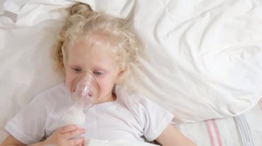 Kıvırcık sarı saçlı tatlı küçük kız yatakta yatıyor, hasta beş bantlı kız nebulizatörle nefes alıyor, bronşit ve çocuklarda akciğer hastalığı tedavisi görüyor.