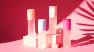 Pembe geometrik podyumlarda parfümlü birkaç sprey şişe üzerinde sallanan bir palmiye yaprağının gölgesi parfüm sunumu için kompozisyon sahnede dört parfüm şişesi, pembe arka plan.
