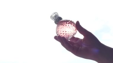 Pencere ve güneş ışığının arka planında parfüm bulunan pembe kristal şişe spreyi. Sert gölgeler, güneş ışığı ve parıltı.