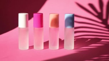 Pembe geometrik podyumlarda parfümlü birkaç sprey şişe üzerinde sallanan bir palmiye yaprağının gölgesi parfüm sunumu için kompozisyon sahnede dört parfüm şişesi, pembe arka plan.