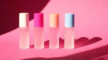 Pembe geometrik podyumlarda parfümlü birkaç sprey şişe üzerinde sallanan bir palmiye yaprağının gölgesi parfüm sunumu için kompozisyon sahnede dört parfüm şişesi, pembe arka plan.
