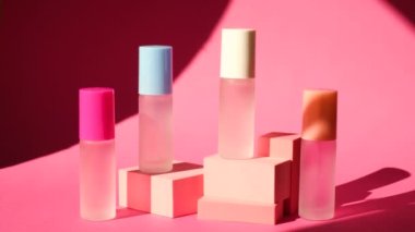 Pembe geometrik podyumlarda parfümlü birkaç sprey şişe üzerinde sallanan bir palmiye yaprağının gölgesi parfüm sunumu için kompozisyon sahnede dört parfüm şişesi, pembe arka plan.