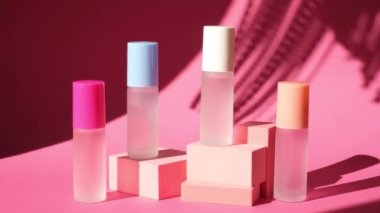 Pembe geometrik podyumlarda parfümlü birkaç sprey şişe üzerinde sallanan bir palmiye yaprağının gölgesi parfüm sunumu için kompozisyon sahnede dört parfüm şişesi, pembe arka plan.
