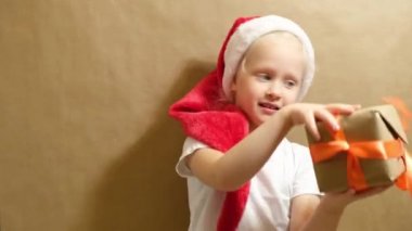 Kırmızı şapkalı şirin bir kız hediyeyle oynuyor, turuncu kurdeleli hediye kutusu ve kurdele, noel hediyeleri konsepti.