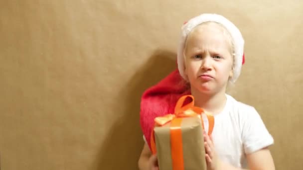 Linda chica en una gorra roja jugando con un regalo, caja de regalo con cinta naranja y arco, concepto de regalos de Navidad — Vídeos de Stock