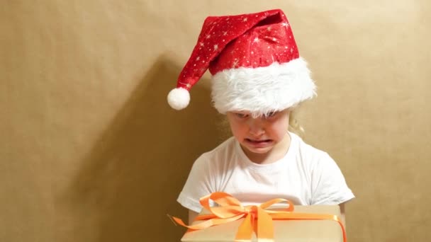 Cute girl in a red cap playing with a gift, gift box with orange ribbon and bow, christmas gifts concept — Stock Video