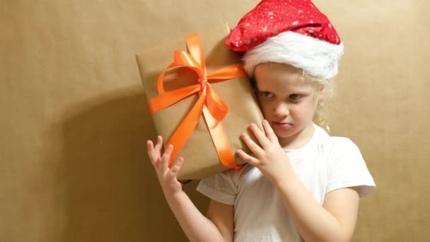 Linda chica en una gorra roja jugando con un regalo, caja de regalo con cinta naranja y arco, concepto de regalos de Navidad — Vídeos de Stock