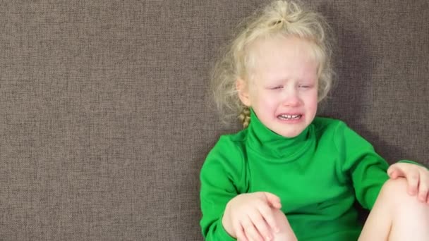 Cute little girl in a green sweater crying while sitting on the couch — Stock Video