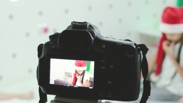 ティーン女の子ブロガーでSanta hat座っている上のベッドと話上のカメラ. — ストック動画