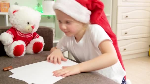 可爱的白种人女孩 戴着圣诞礼帽 写信给圣诞老人 圣诞气氛 平安夜 节日准备 圣诞气氛和装饰 — 图库视频影像