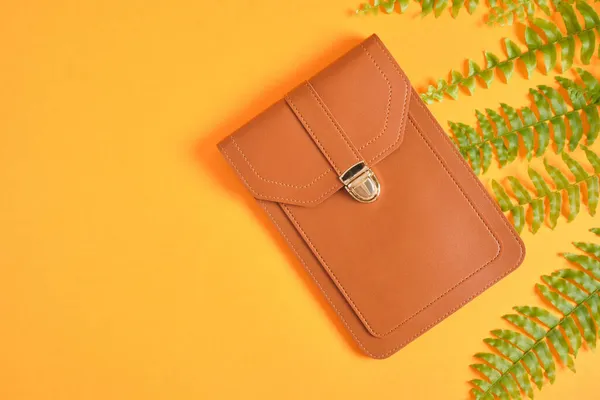 phone and wallet bag and fern on orange background, eeo vegan leather from plants concept copy space top view