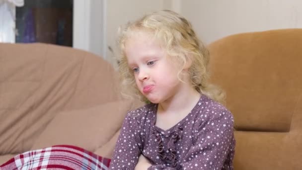 Schattig meisje met krullend blond haar was beledigd en opgeblazen haar wangen, een ontevreden blanke meisje op een stoel — Stockvideo