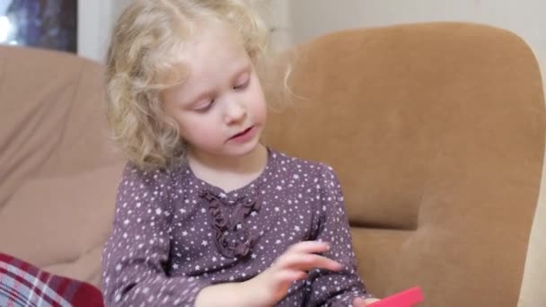 Menina bonito com cabelo louro encaracolado brincando com pop it pipe brinquedo sentado em uma cadeira — Vídeo de Stock