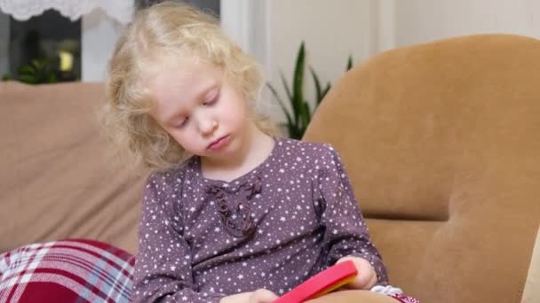 Gadis cantik dengan rambut pirang keriting bermain dengan pop itu mainan pipa duduk di kursi — Stok Video