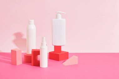 Pembe arka plandaki pembe geometrik podyumlardaki birkaç farklı beyaz plastik şişe ve tüp kozmetik şişeleri taklit ediyor. Kimlik modelleme konsepti.