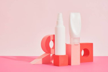 Pembe arka plandaki pembe geometrik podyumlardaki birkaç farklı beyaz plastik şişe ve tüp kozmetik şişeleri taklit ediyor. Kimlik modelleme konsepti.