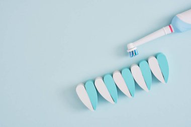 Elektrikli diş fırçası ve mavi arkaplandaki dişlerin yaratıcı bileşimi, diş fırçalarının ağız boşluğunu temizlemede daha etkili ve çevre dostu.