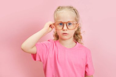 Pembe tişörtlü, burnuna gözlük takan beyaz bir anaokulu öğrencisinin portresi, çocuk göz doktoru konsepti, okula geri dönüyor.