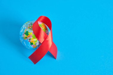 Dünya AIDS Günü. Dayanışmanın sembolü kırmızı bir kurdele ve oyuncak küre mavi arka plan 1 Aralık Dünya Yardım Günü