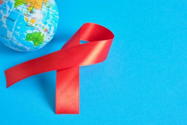Dünya AIDS Günü. Dayanışmanın sembolü kırmızı bir kurdele ve oyuncak küre mavi arka plan 1 Aralık Dünya Yardım Günü