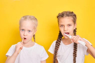 Sarı arka planda dişlerini fırçalayan neşeli kızlar, yeni yürümeye başlayan çocuklar ve genç kızlar, elektrikli ya da bambu fırçası konsepti, çocuklar için diş fırçası