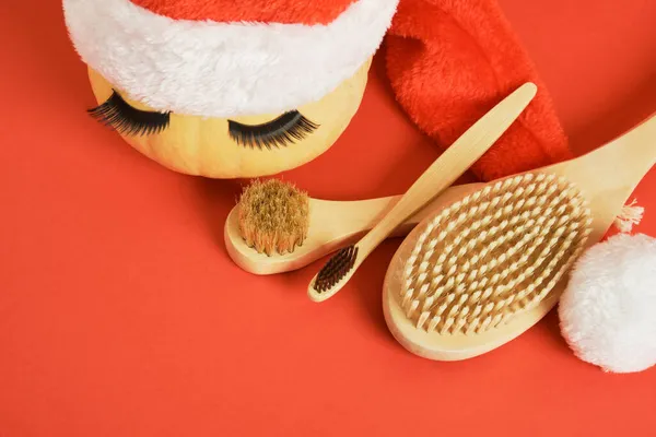 bamboo toothbrush, wooden massage brushes, pumpkin with false eyelashes and towel on gray background, peeling with dry brush massage