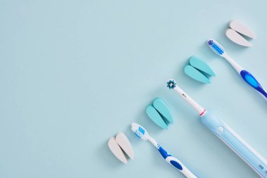 Mavi arka planda elektrikli ve plastik diş fırçaları, diş fırçalarının ağız boşluğunu temizlemede ve çevre dostu çalışmada daha etkilidir.