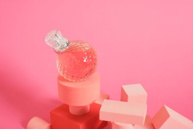 Kristal cam parfüm şişesi ve pembe arkaplan fotokopi alanı üzerinde geometrik podyumlar