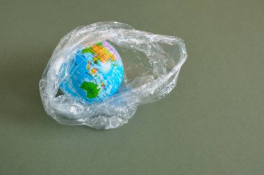 Yeşil arka planda izole edilmiş polietilen plastik tek kullanımlık pakette Dünya tiy modeli. Polietilen plastik atık ile çevre kirliliği kavramı, ekolojik sorunlar. Plastik kirliliğini durdur
