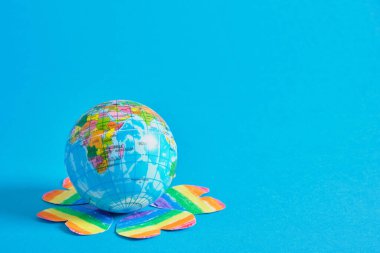 Gezegen şeklinde bir oyuncak topu ve lgbtq topluluğunun renklerine boyanmış çok sayıda kalp, gurur kavramı mavi arka plan