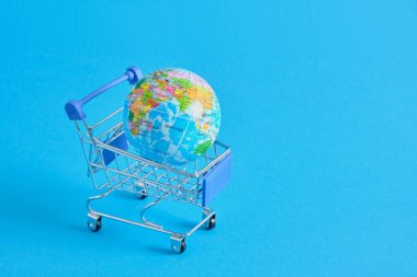 Mavi arka planda süpermarket alışveriş arabasında bir dünya gezegeni. Dünya gezegeni şeklinde uzay alışveriş arabalarını ve oyuncak toplarını kopyala