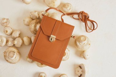 Akıllı telefon ve kredi kartları için küçük kahverengi çanta ve bej arka planda şampiyonlar, vegan deri konsepti, hayvan derisine alternatif, mantar miselyumundan deri