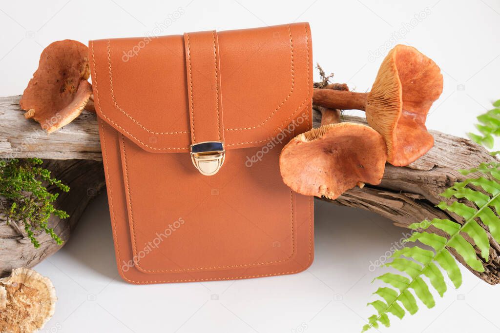 brown bag made of eco leather, driftwood, toadstools mushrooms and fern on a gray background, genuine leather from mushroom mycelium concept