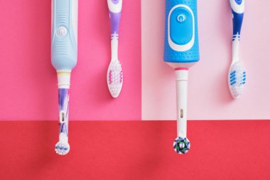 Pembe ve kırmızı arka planda farklı diş fırçaları, elektrikli diş fırçaları veya plastik diş fırçaları, çevre dostu yaşam tarzı konsepti, diş fırçalama etkinliği