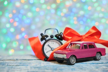Minyatür mor retro araba modeli, ahşap bir yüzeyde kırmızı kurdele ve alarm saati, kopyalama alanı, arka planda bokeh, noel ışıkları.